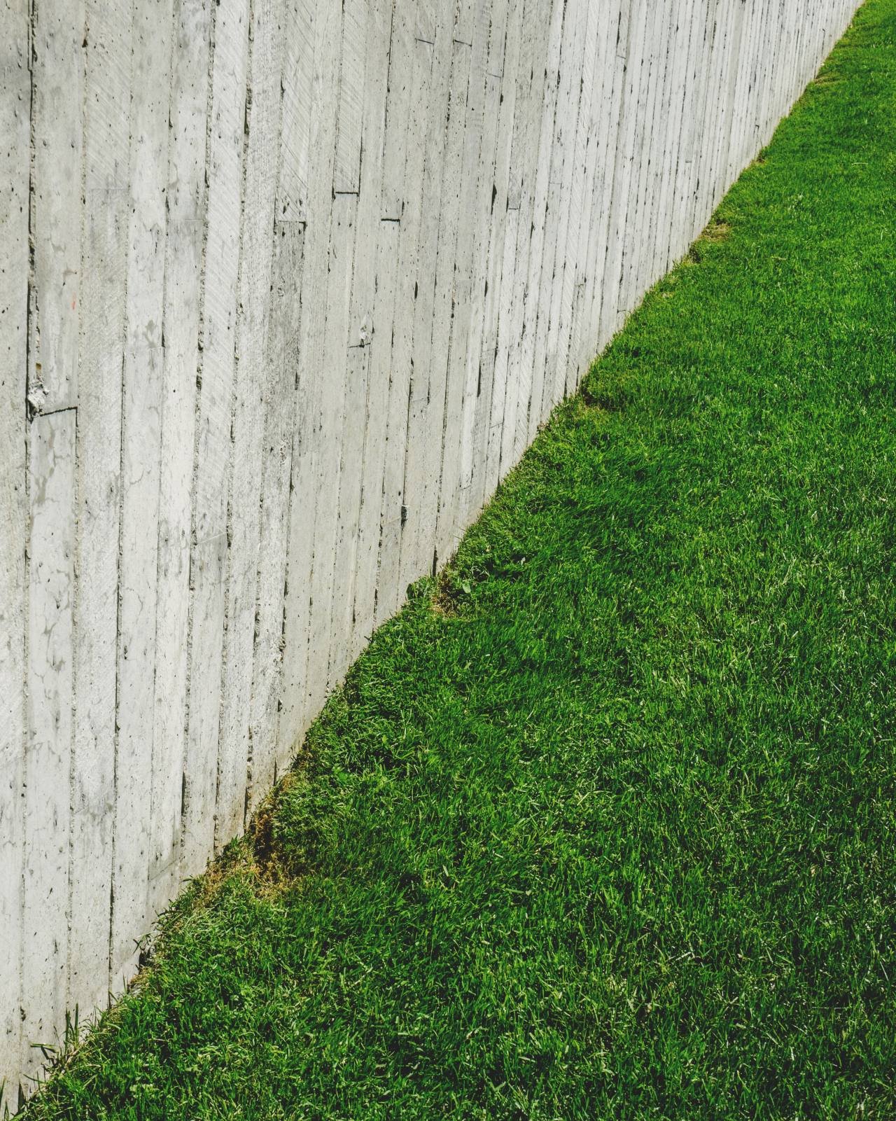 A bright green lawn meeting a board-formed concrete wall in one clean diagonal line