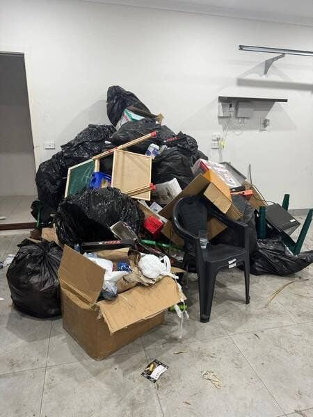 A pile of household rubbish — bin bags, boxes, a whiteboard and a plastic chair — in an empty room before pick-up